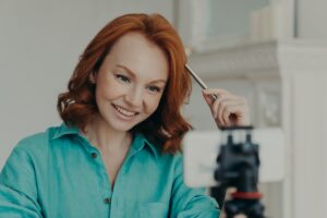 Happy redhead woman records video on webcam, talks to subscribers, has personal blog